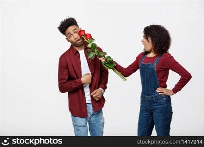 Portrait of a disappointed young woman holding red rose with while standing and angry on her boyfriend isolated over white background.. Portrait of a disappointed young woman holding red rose with while standing and angry on her boyfriend isolated over white background