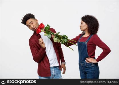 Portrait of a disappointed young woman holding red rose with while standing and angry on her boyfriend isolated over white background.. Portrait of a disappointed young woman holding red rose with while standing and angry on her boyfriend isolated over white background