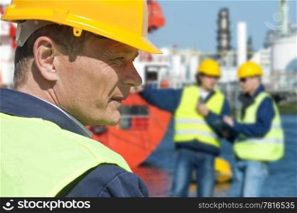 Portrait of a docker in front of a harbor scene with two of his coworkers out of focus in the background