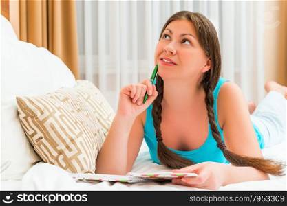 Portrait of a dreamy brunette is located on the bed with a notepad
