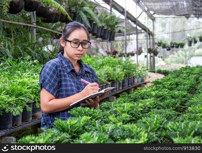 Portrait of a farmer Asian woman at work in greenhouse with notebook examines the growing seedlings on the farm and diseases in greenhouse.