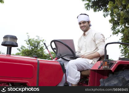 Portrait of a farmer with a laptop sitting on a tractor