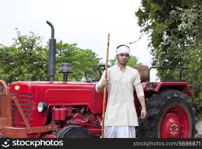 Portrait of a farmer with a stick standing next to tractor