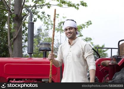 Portrait of a farmer with a stick standing next to tractor