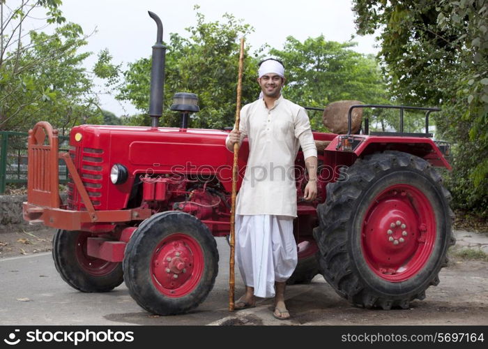 Portrait of a farmer with a stick standing next to tractor