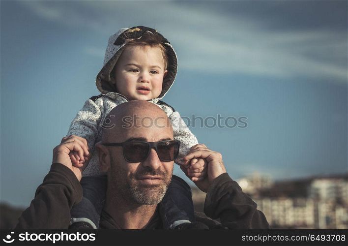 Portrait of a father carrying his cute little son on shoulders, baby and daddy with pleasure spending time together outdoors, happy family life. Father carrying his little son