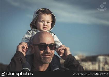 Portrait of a father carrying his cute little son on shoulders, baby and daddy with pleasure spending time together outdoors, happy family life. Father carrying his little son