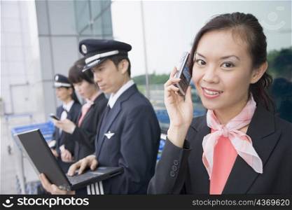 Portrait of a female cabin crew talking on a mobile phone with a pilot using a laptop in the background