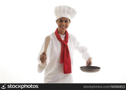 Portrait of a female chef holding frying pan and wooden spatula isolated over white background