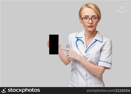 Portrait of a female doctor or nurse holding and showing mobile phone with blank screen.. Portrait of a female doctor or nurse holding and showing mobile phone with blank screen