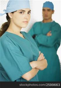 Portrait of a female doctor standing with her arms crossed and a male doctor standing in the background