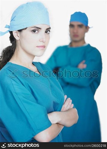 Portrait of a female doctor standing with her arms crossed and a male doctor standing in the background