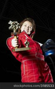 Portrait of a female go-cart racer showing her trophy and smiling