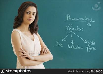 Portrait of a female professor with arms crossed standing against blue board