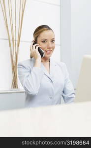 Portrait of a female receptionist talking on a mobile phone in front of a computer