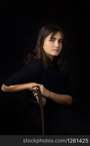 Portrait of a fifteen-year-old girl on a black background, a girl clouded on the back of a chair