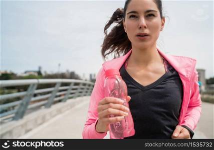Portrait of a fitness woman running and holding a bottle of water outdoors in the street. Sport and healthy lifestyle.