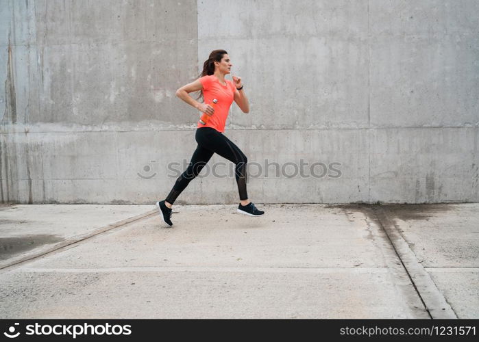 Portrait of a fitness woman running on the street against grey background. Sport and healthy lifestyle.