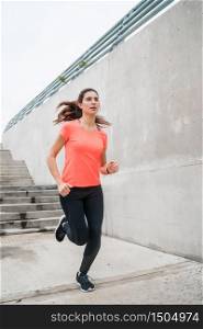 Portrait of a fitness woman running on the street against grey background. Sport and healthy lifestyle.
