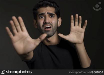Portrait of a frightened young man looking at the camera and gesturing with his hands