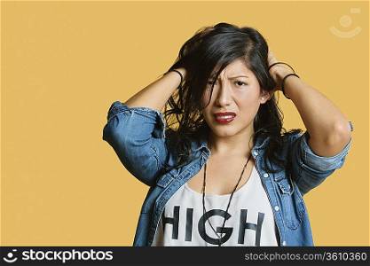 Portrait of a frustrated young woman with hands in hair over colored background