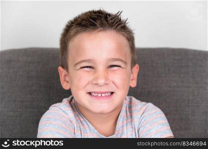 Portrait of a Funny little boy smiling and laughing looking at camera sitting on the couch at home. Concept of a happy childhood. High quality photography. Portrait of a Funny little boy smiling and laughing looking at camera sitting on the couch at home. Concept of a happy childhood.