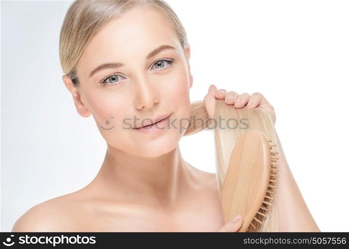 Portrait of a gentle blond female combing her hair isolated on grey white background, treatment in spa salon, healthy hair and skin