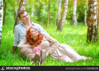 Portrait of a gentle young couple relaxing in a fresh green spring park, sitting on a field between birch trees, enjoying wedding day