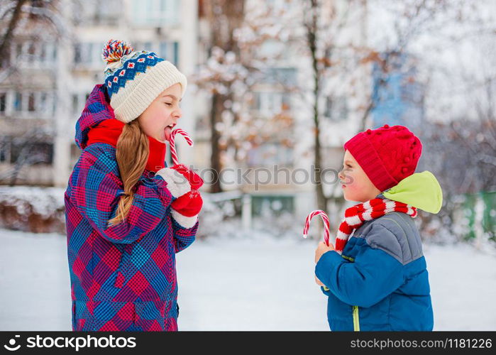 Portrait of a girl and a boy with Christmas sweets in their hands on a winter street. Brother and sister have fun during the holidays.. Portrait of a girl and a boy with Christmas sweets in their hands on a winter street.