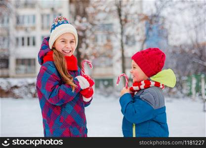 Portrait of a girl and a boy with Christmas sweets in their hands on a winter street. Brother and sister have fun during the holidays.. Portrait of a girl and a boy with Christmas sweets in their hands on a winter street.