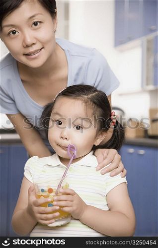 Portrait of a girl drinking juice and her mother standing behind her