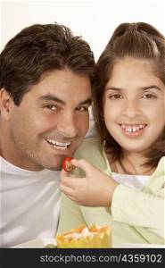 Portrait of a girl feeding her father a strawberry