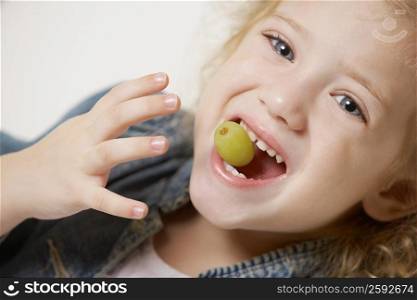 Portrait of a girl holding a grape between her teeth