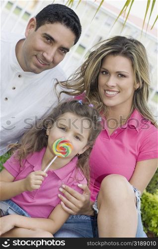 Portrait of a girl holding a lollipop with her parents in a park