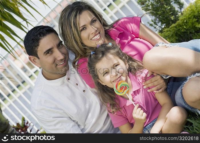 Portrait of a girl holding a lollipop with her parents in a park