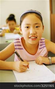 Portrait of a girl holding a pen on a notepad in the classroom
