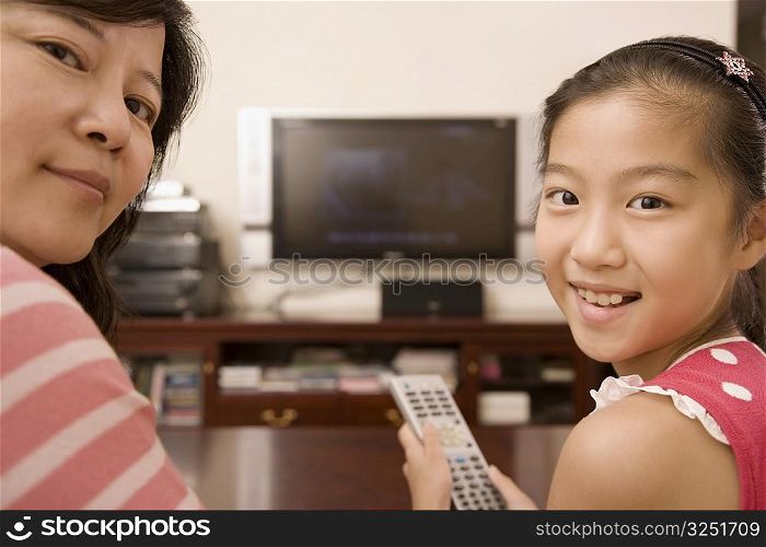 Portrait of a girl holding a remote control and smiling with her mother
