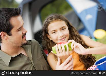 Portrait of a girl holding a watermelon with her father looking at her