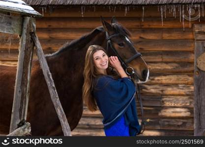 Portrait of a girl hugging a horse against the background of a wall of logs
