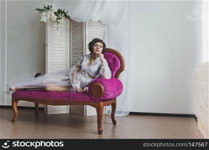 Portrait of a girl in a light dress in the Studio.. The girl in the translucent dress reclines on the sofa 6356.