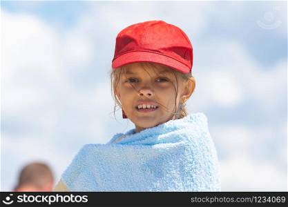 Portrait of a girl in a red cap wrapped in a towel against the sky