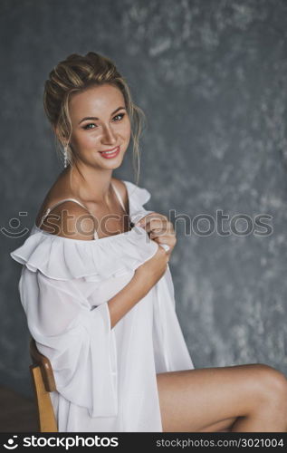 Portrait of a girl in the room on the background of gray wall.. A beautiful portrait of a girl in a white gown with makeup and hair 137.