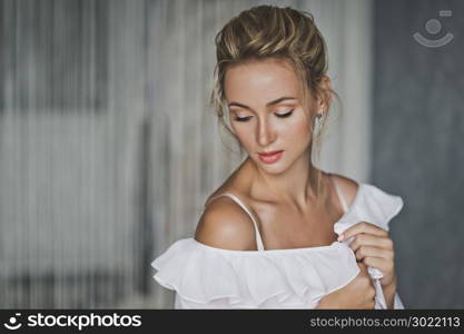 Portrait of a girl in the room on the background of gray wall.. A beautiful portrait of a girl in a white gown with makeup and hair 138.