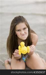 Portrait of a girl kneeling on the beach and holding a toy