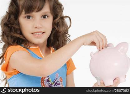 Portrait of a girl putting a coin into a piggy bank