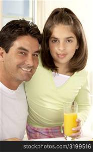 Portrait of a girl sitting and holding a glass of orange juice with her father