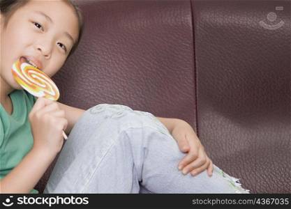 Portrait of a girl sitting on a couch and licking a lollipop