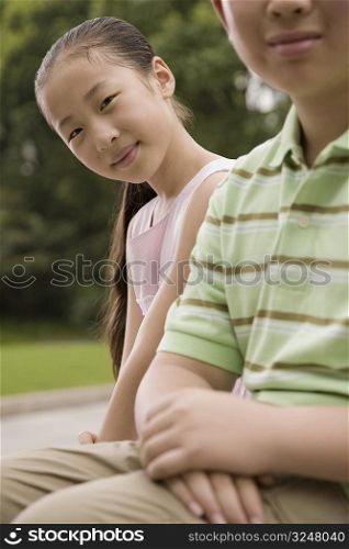 Portrait of a girl sitting with her brother in a park