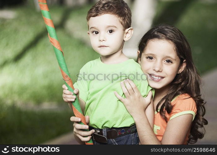 Portrait of a girl smiling and her brother holding a stick