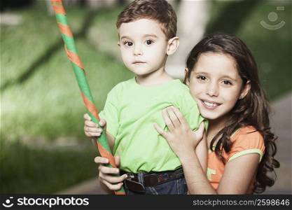 Portrait of a girl smiling and her brother holding a stick